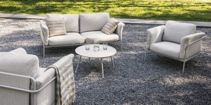 „Marinelli Beige“ lauko baldų komplektas su sofa, foteliais ir apvaliu stalu, pastatytas šviesioje terasoje.