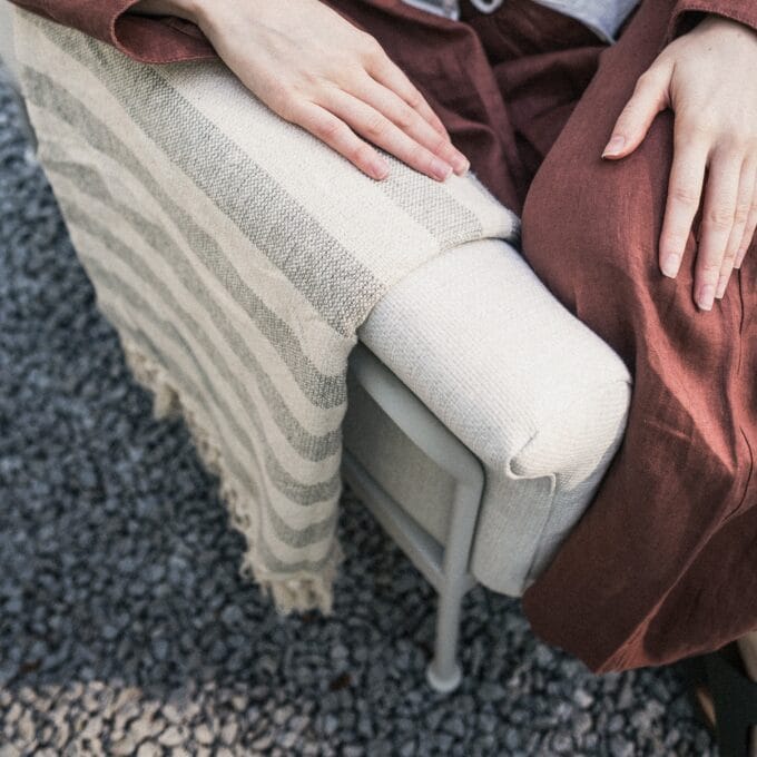 „Marinelli Beige“ lauko baldų komplektas su sofa, foteliais ir apvaliu stalu, pastatytas šviesioje terasoje.